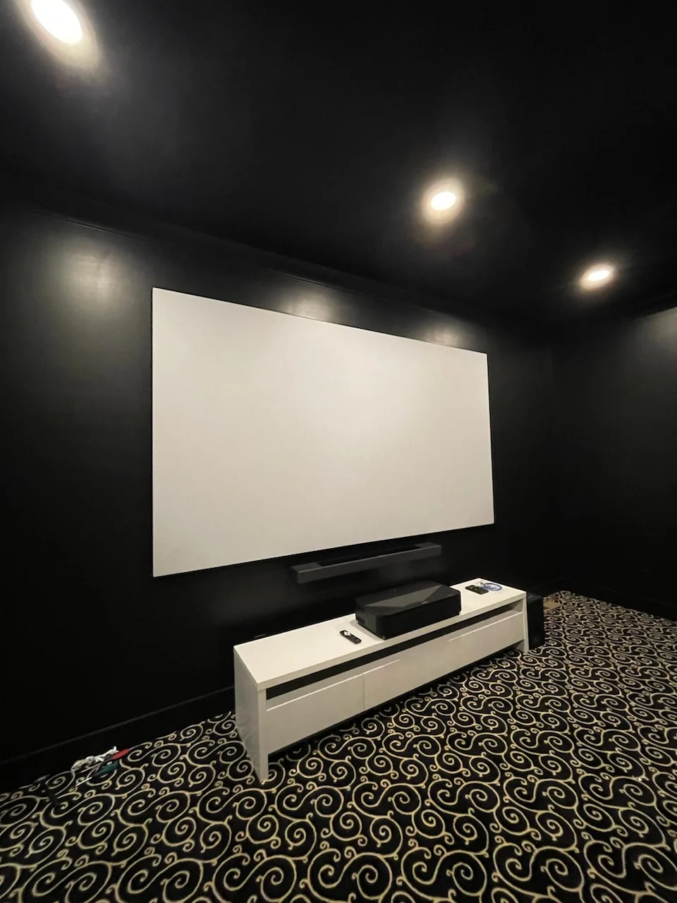 A Nice Guys dark theater with a large projection screen, soundbar and ultra-short-throw projector