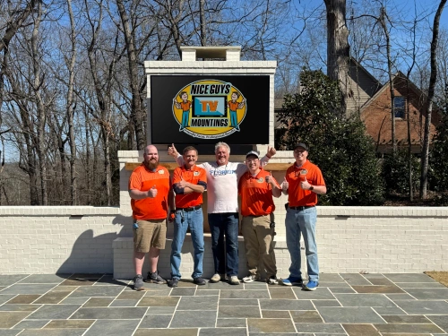 The Nice Guys team beside an outdoor TV installation above a patio fireplace